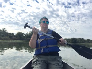 A fat woman in a life vest, teal hair, and sunglasses, rowing a canoe